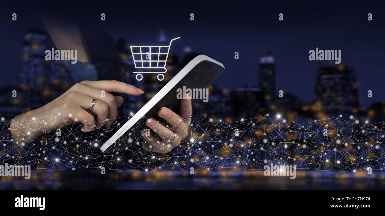 Internet Carrello Web Store Online Acquista concetto di e-commerce. Mano touch tablet bianco con ologramma digitale carrello segno sulla città scuro sfondo sfocato. Il co Foto Stock