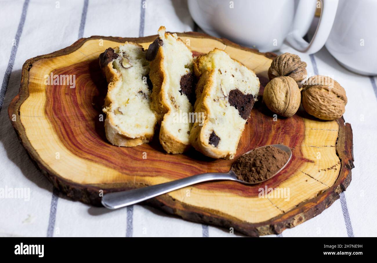 Fettine di torta in legno con noci e cucchiaio di cacao in polvere Foto Stock