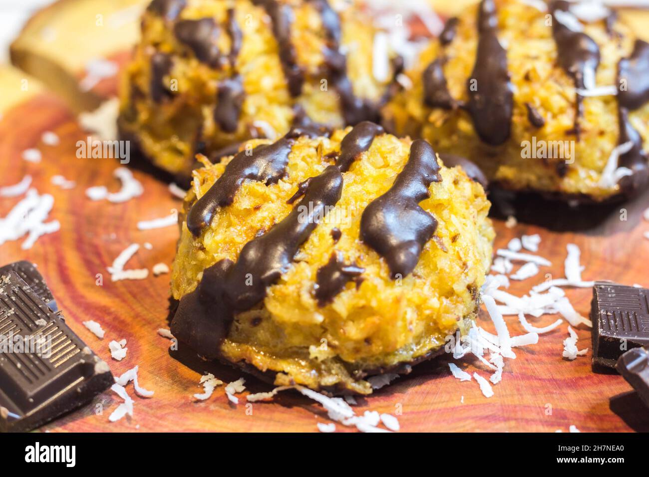 Amaretti di cocco con gocce di cioccolato scuro serviti su legno di ciliegio guarnito con pezzi di cioccolato e Shavings di cocco, fuoco selettivo Foto Stock