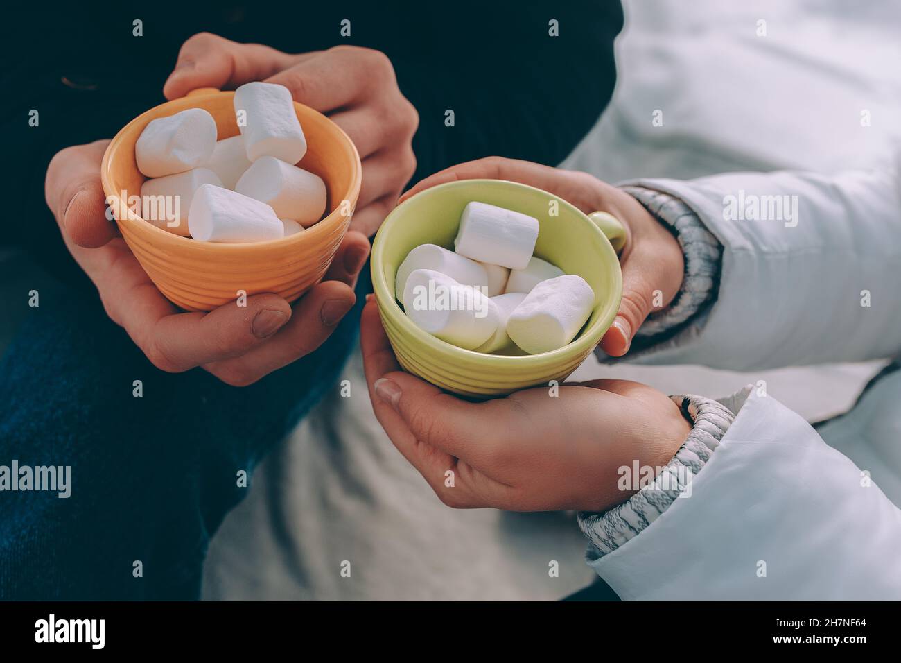 le mani di coppia in primo piano tengono le tazze verdi e gialle con marshmallow Foto Stock