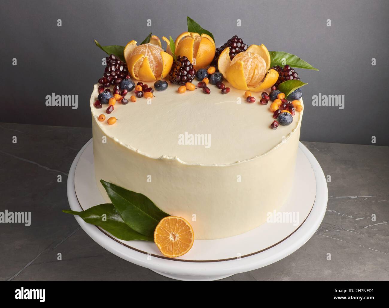 Gustosa torta bianca decorata con arance melograne sfondo grigio mirtillo Foto Stock
