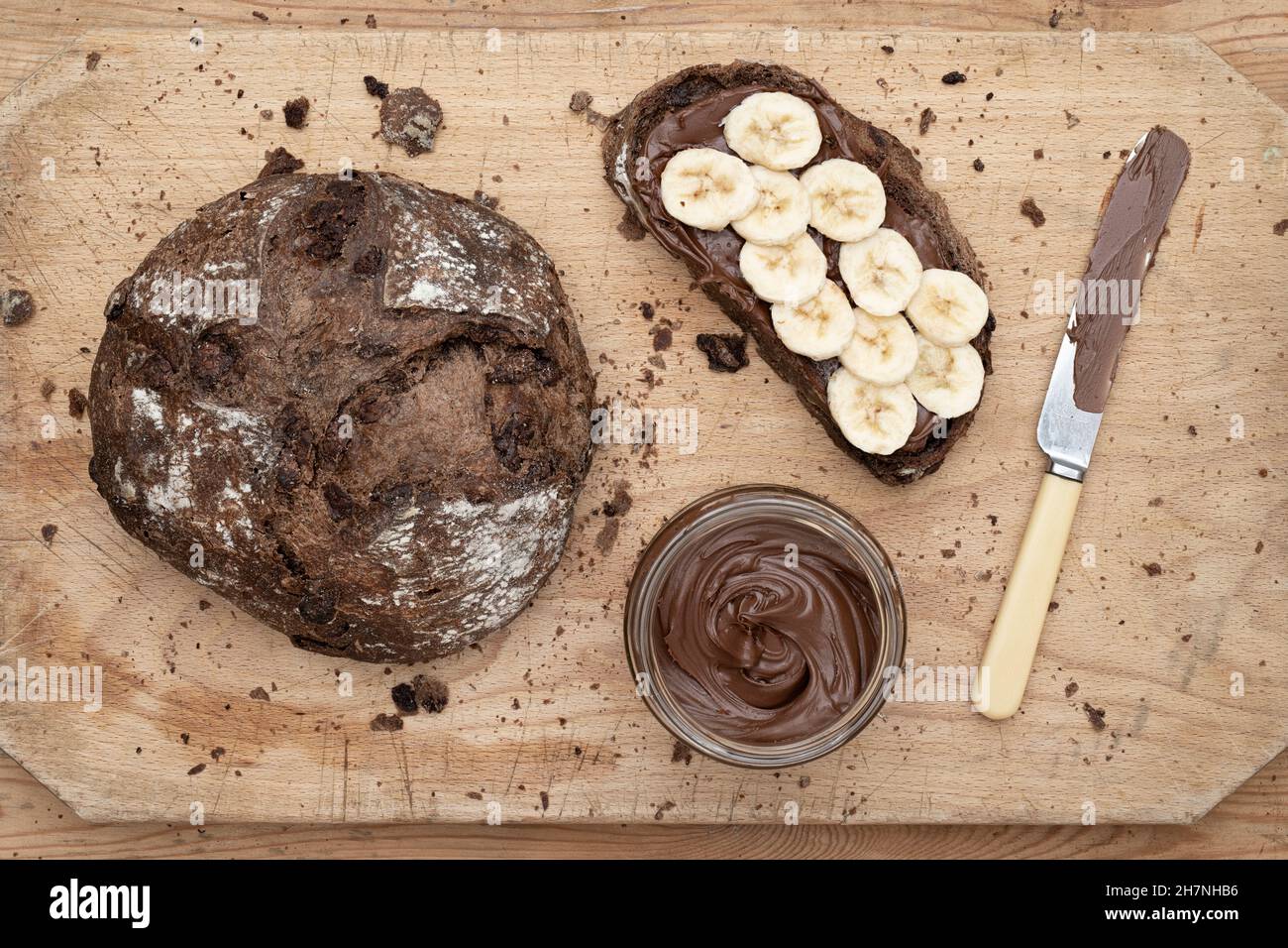 Pane di pasta al cioccolato con crema di nocciole al cioccolato e banana affettata su un asse di legno Foto Stock