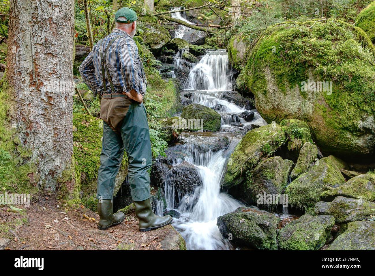 Un zaino in spalla si erge di fronte ad una piccola cascata e gode il suono dell'acqua e del silenzio nella foresta. Foto Stock