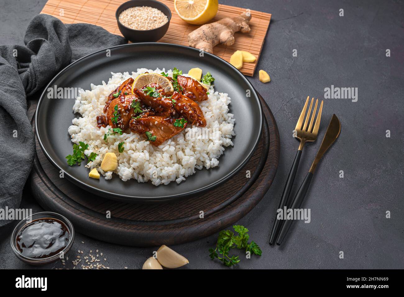 Pollo Teriyaki con riso e semi di sesamo in un piatto nero. Foto Stock