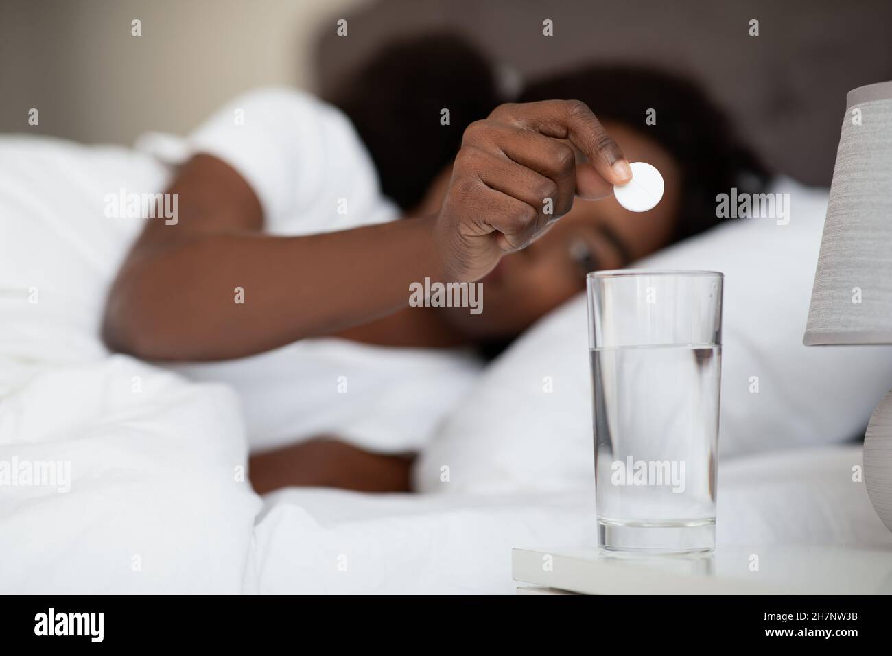 Donna nera che stesa a letto, sciogliendo la medicina in acqua Foto Stock
