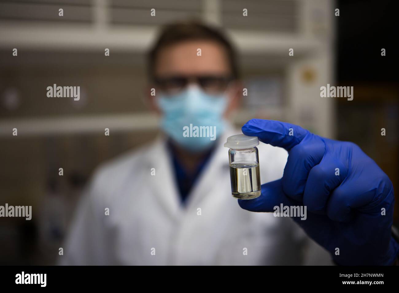 Test dell'olio di cannabis in laboratorio. Scienziato con una maschera con guanti per mano e viso che contiene una fiala di olio CBD Foto Stock