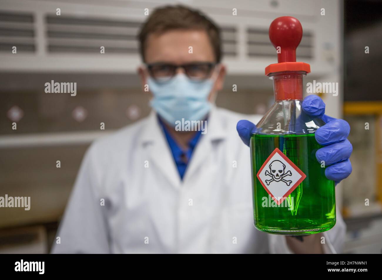 Scienziato che indossa un camice da laboratorio bianco che contiene un pallone di sostanza chimica tossica verde. Foto Stock