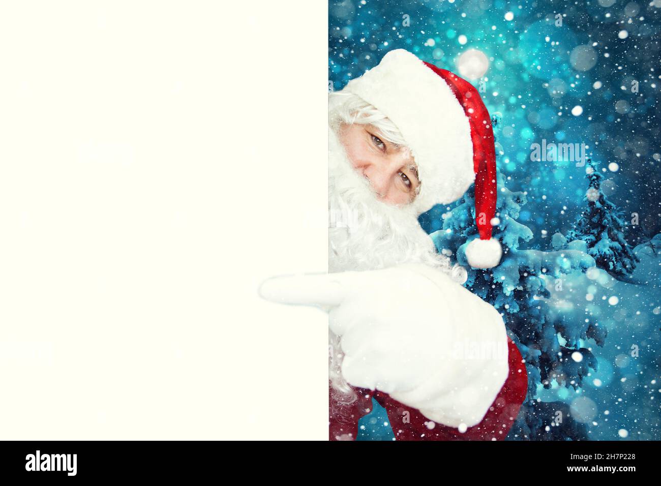 Autentico Babbo Natale che indica un poster bianco vuoto con spazio per la copia. Sullo sfondo, una foresta innevata d'inverno. Natale pubblicità concetto Foto Stock