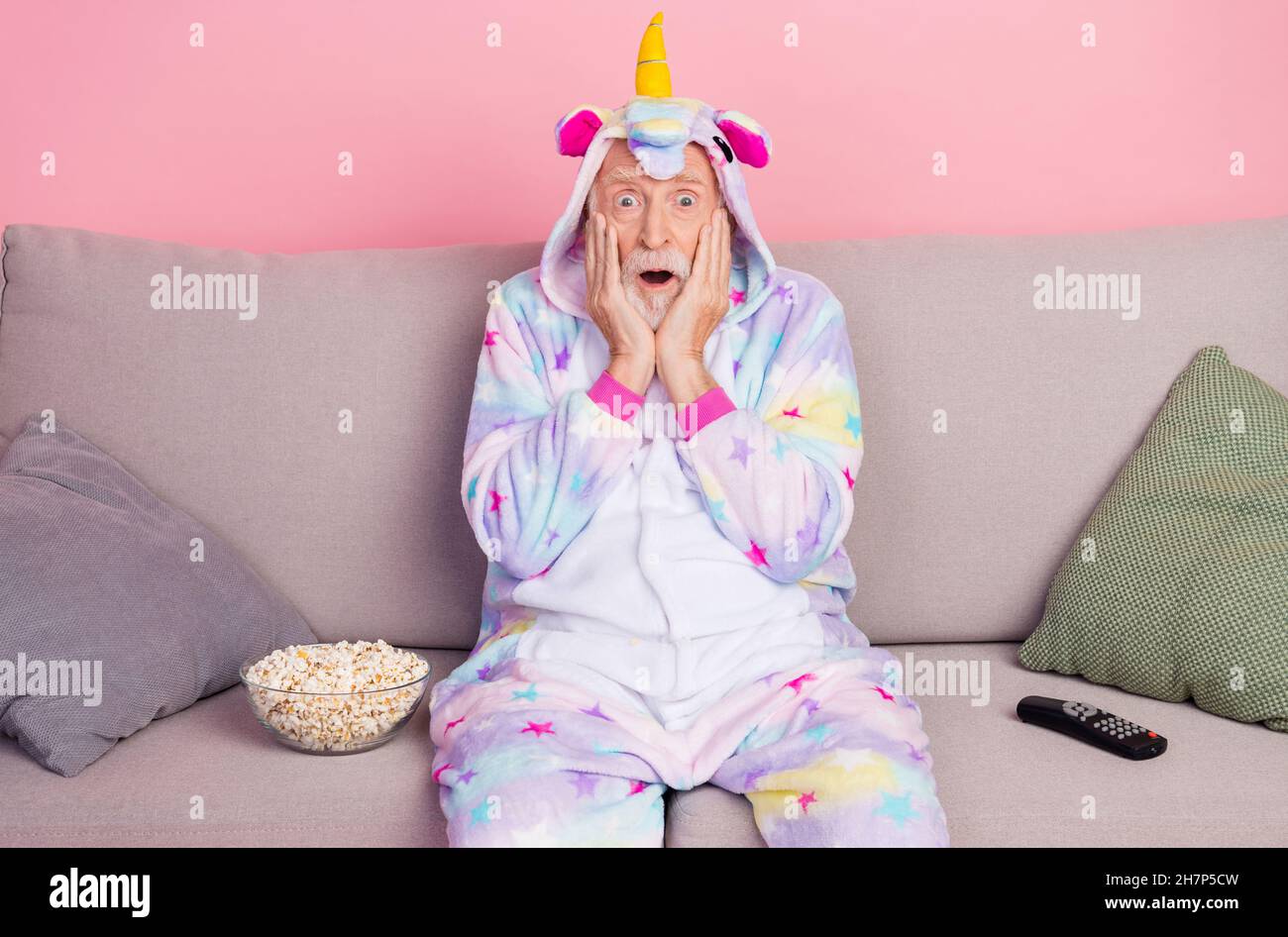 Ritratto di attraente uomo terrorizzato grigio-capelli seduti su divano guardando il video horror isolato su sfondo rosa Foto Stock