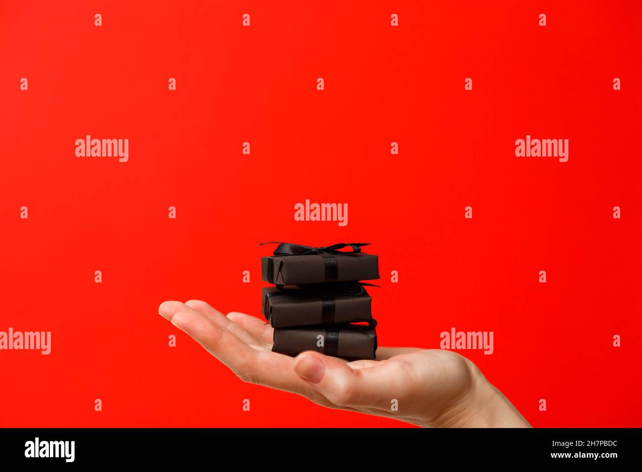 Donna mano che tiene piccole scatole regalo nere con nastri neri su sfondo rosso brillante ricco Foto Stock