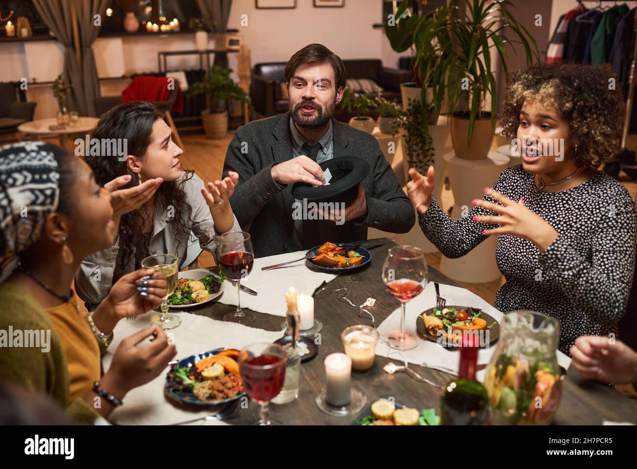 Gruppo di amici seduti al tavolo da pranzo che parlano e giocano durante una festa a cena Foto Stock