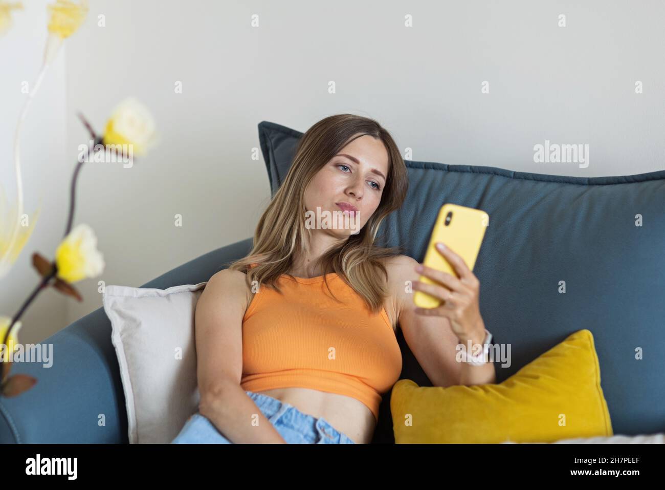 Infelice giovane donna bionda caucasica che si rilassa a casa da sola, seduto sul divano in una comoda posa, blogger che condivide buone notizie sui social media via Foto Stock