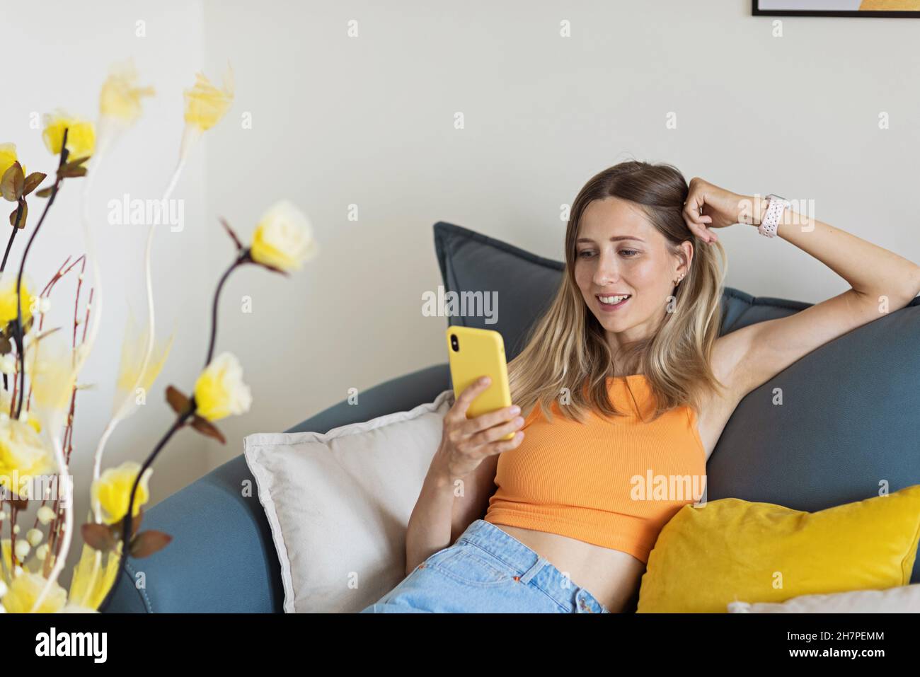 Felice giovane bionda caucasica donna rilassarsi a casa da solo, seduta sul divano in comoda posa, blogger condividere buone notizie sui social media via mobile Foto Stock