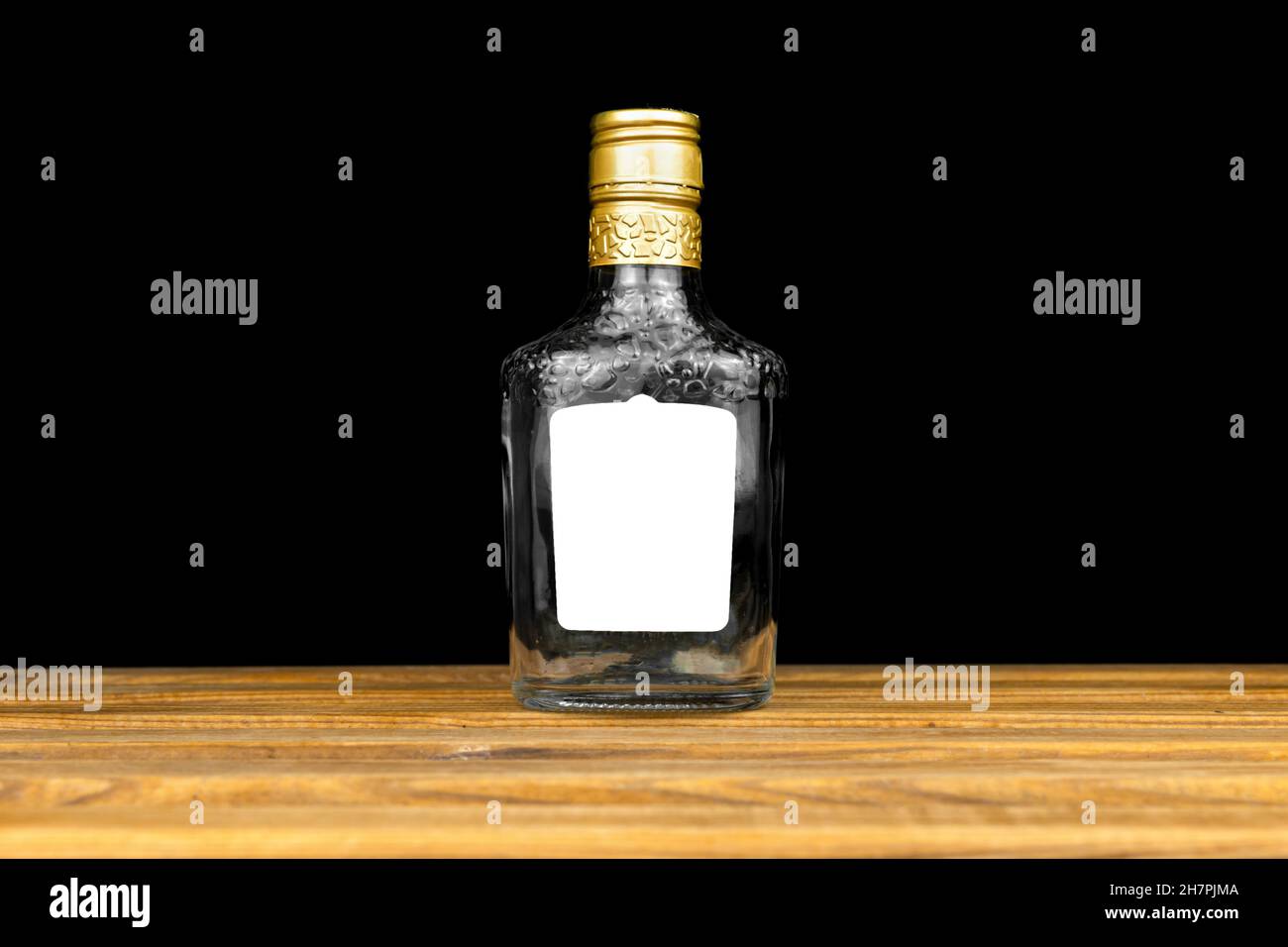 Etichetta mockup su bottiglia di vetro vuota di whiskey, cognac o vodka su sfondo nero, tavolo in legno. Modello, spazio di copia Foto Stock
