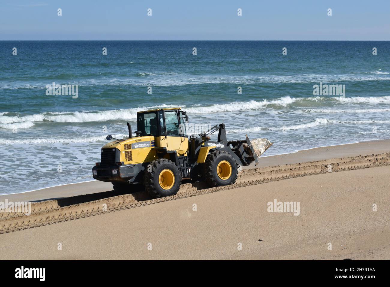 Un trattore trasporta una grande roccia per costruire un muro di mare. Foto Stock