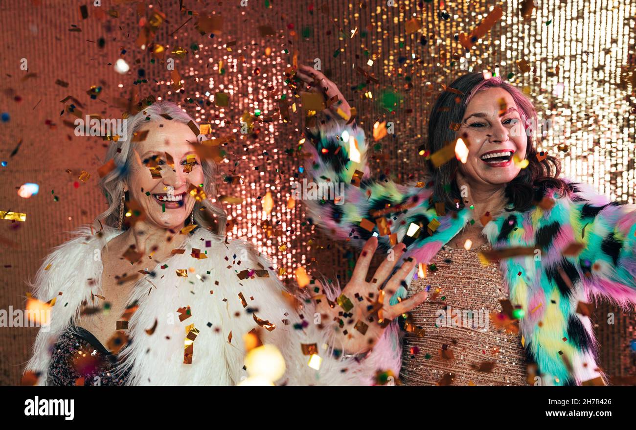Donne anziane in pellicce che festeggiano insieme in studio sotto confetti colorati Foto Stock