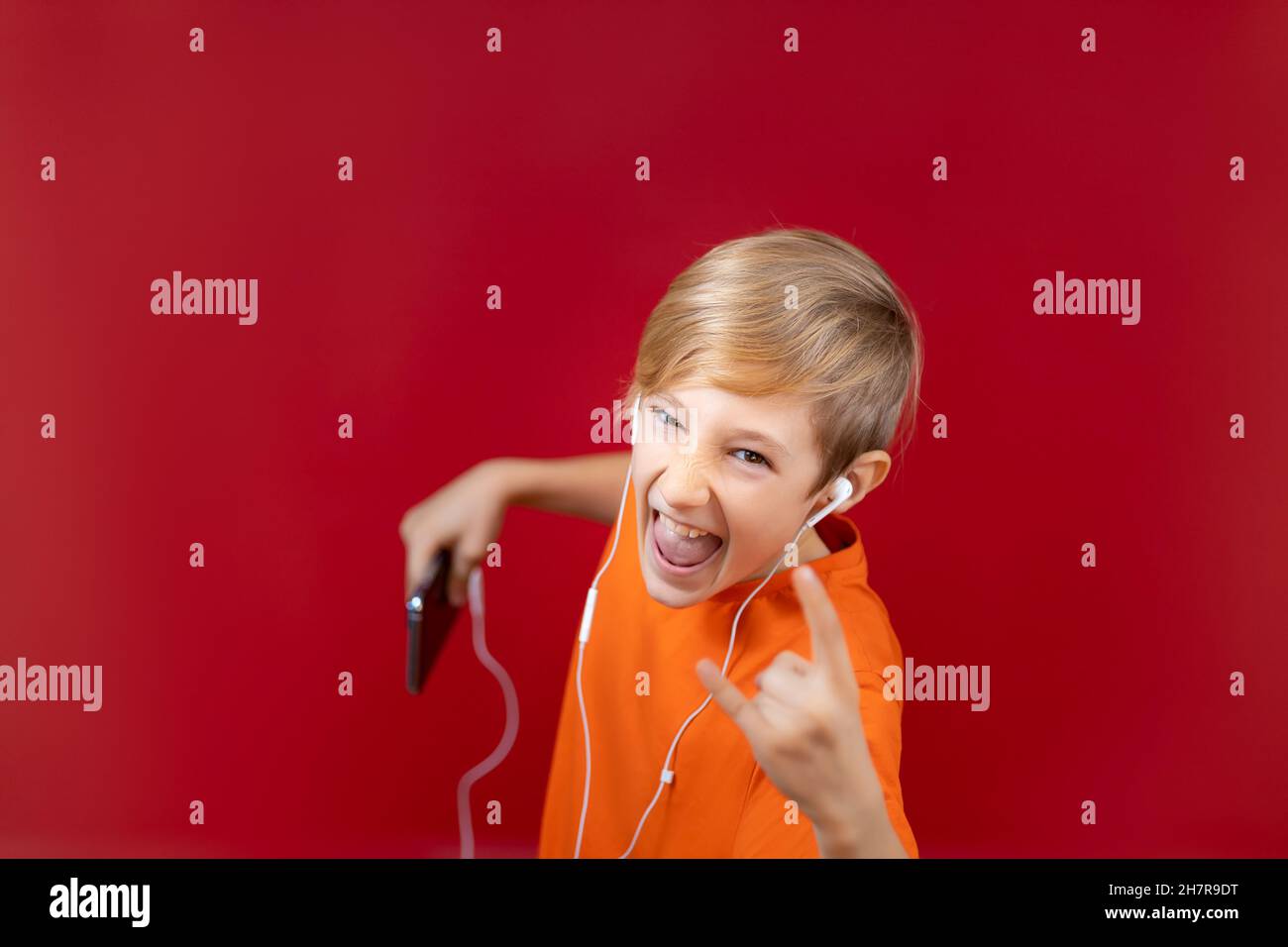 shock ragazzo con telefono in mano, ascolta musica rock pesante e mostra segni di metallo pesante Foto Stock