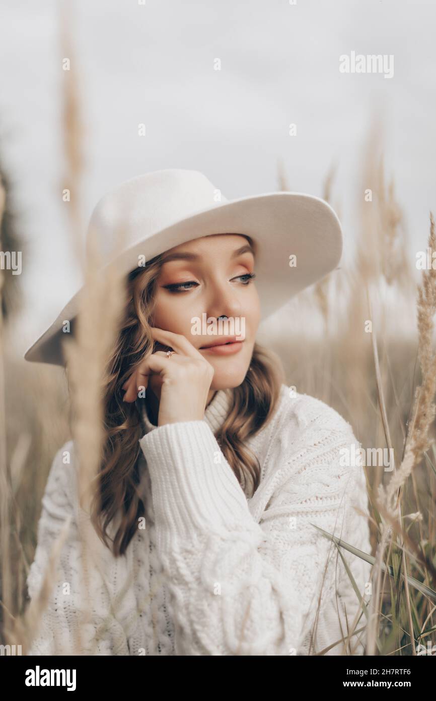 una ragazza bionda in un cappello bianco cammina lungo la riva del mare in un giorno d'autunno Foto Stock