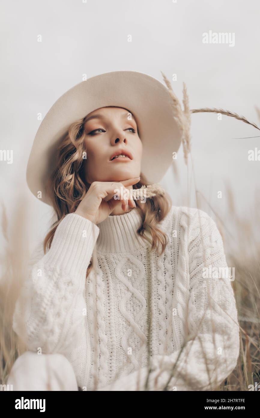 una ragazza bionda in un cappello bianco cammina lungo la riva del mare in un giorno d'autunno Foto Stock