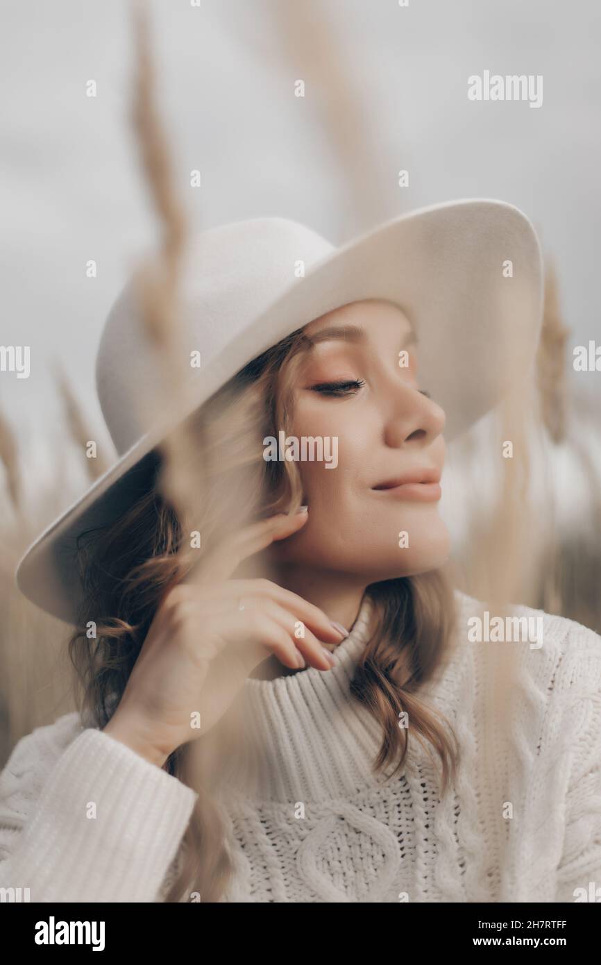 una ragazza bionda in un cappello bianco cammina lungo la riva del mare in un giorno d'autunno Foto Stock