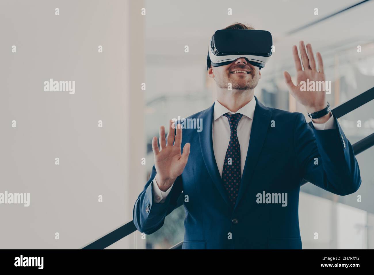 Uomo d'affari in occhiali di realtà virtuale in piedi sulle scale in ufficio e gesturing Foto Stock