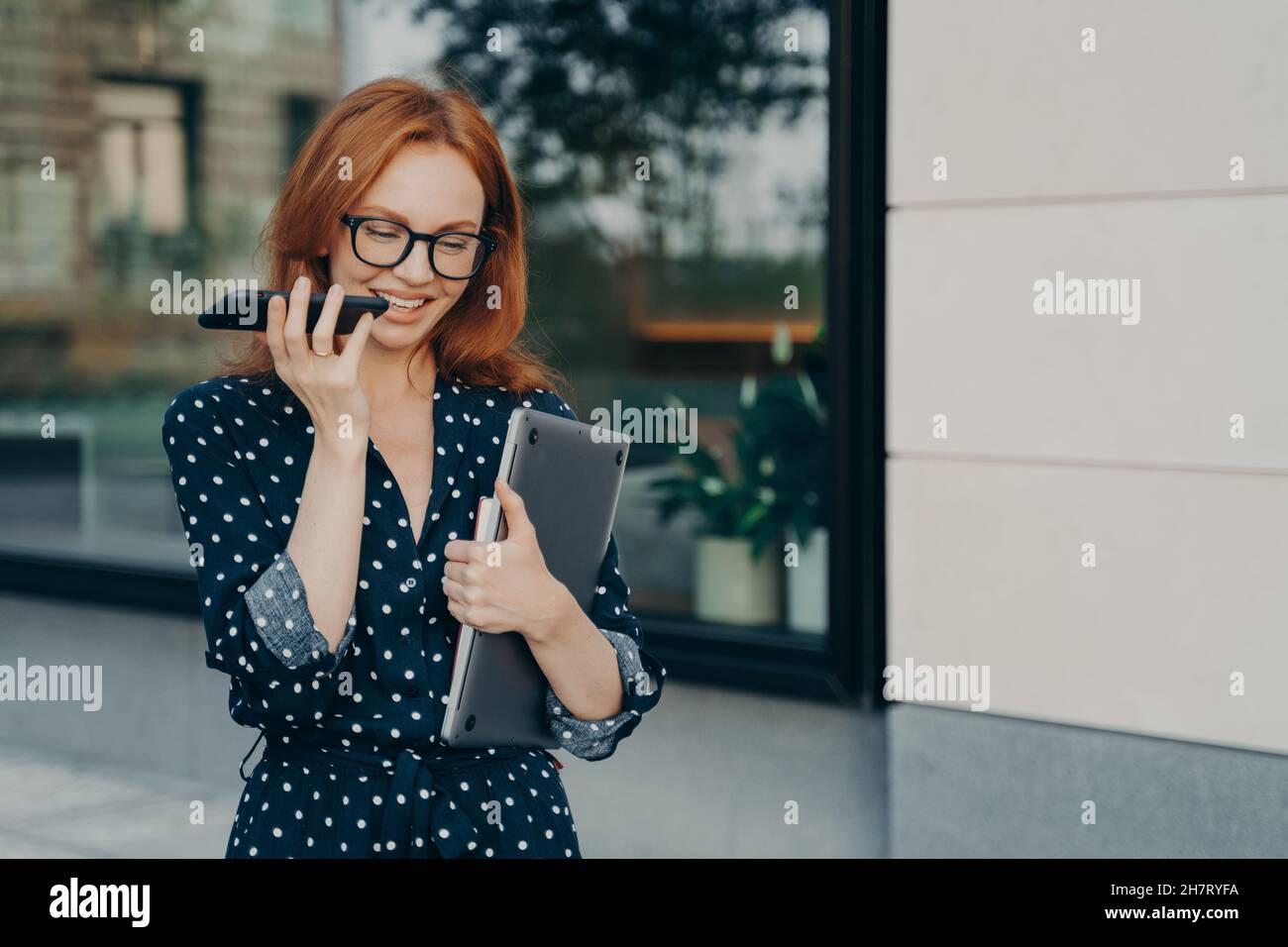 L'imprenditore femminile cammina all'aperto registra i messaggi vocali nei social media tramite smartphone Foto Stock