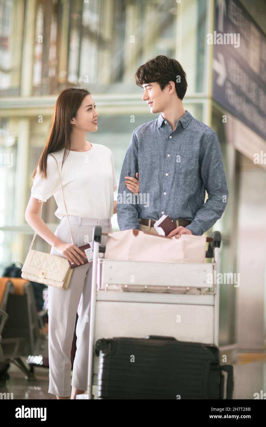 Giovane coppia che spinge i bagagli all'aeroporto Foto Stock