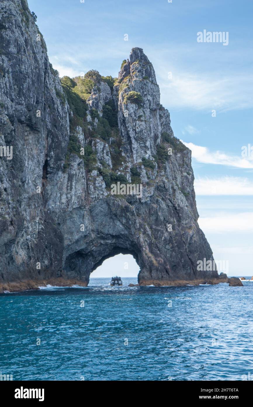 Una singola barca che passa attraverso il Hole in the Rock a Piercy Island, Capo Brett, Bay of Islands Foto Stock