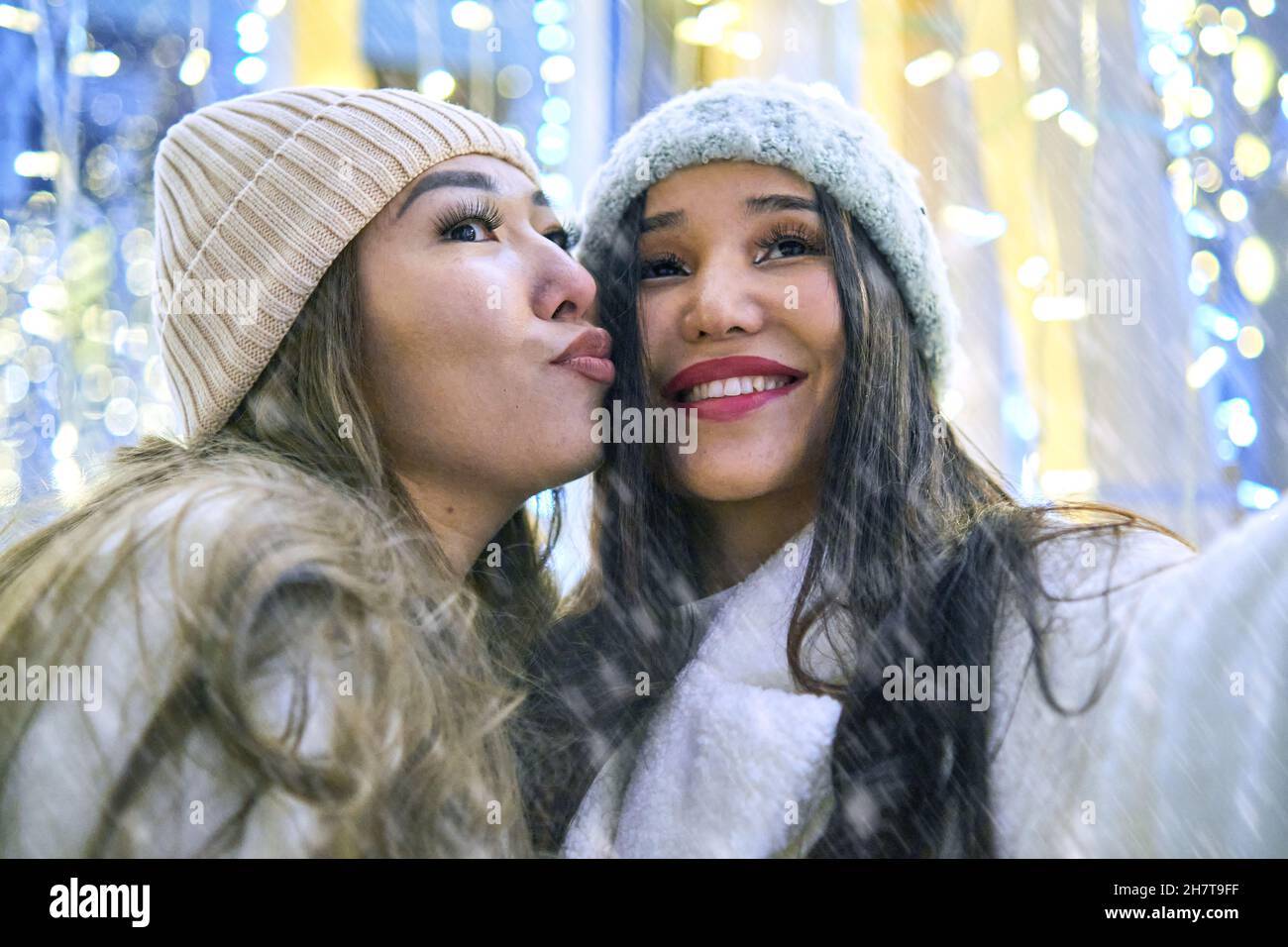 Due ragazze asiatiche in cappotti bianchi stanno avendo divertimento abbracciare, anno nuovo, lampadine Foto Stock