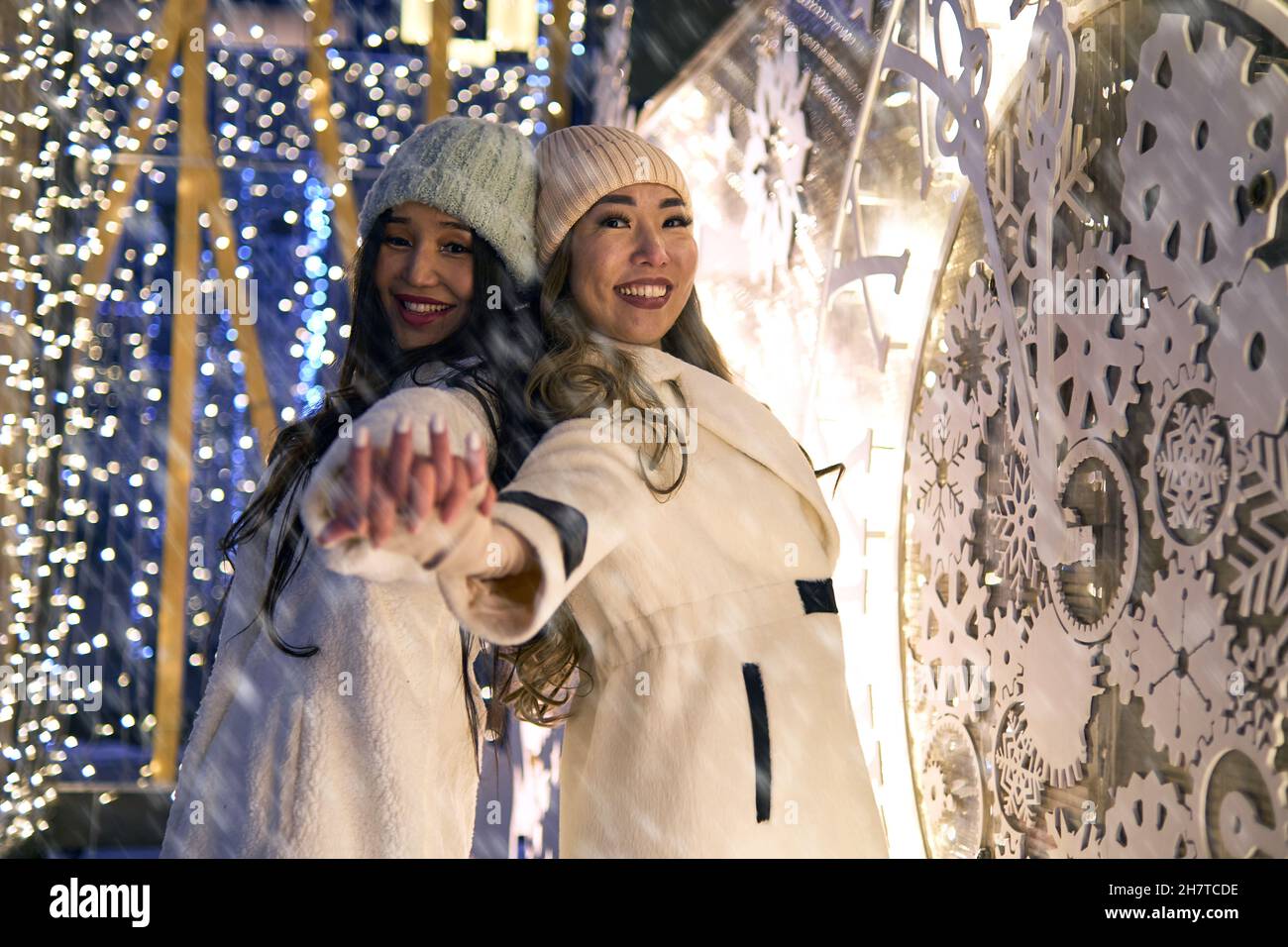 Due ragazze asiatiche in cappotti bianchi stanno avendo divertimento abbracciare, anno nuovo, lampadine Foto Stock