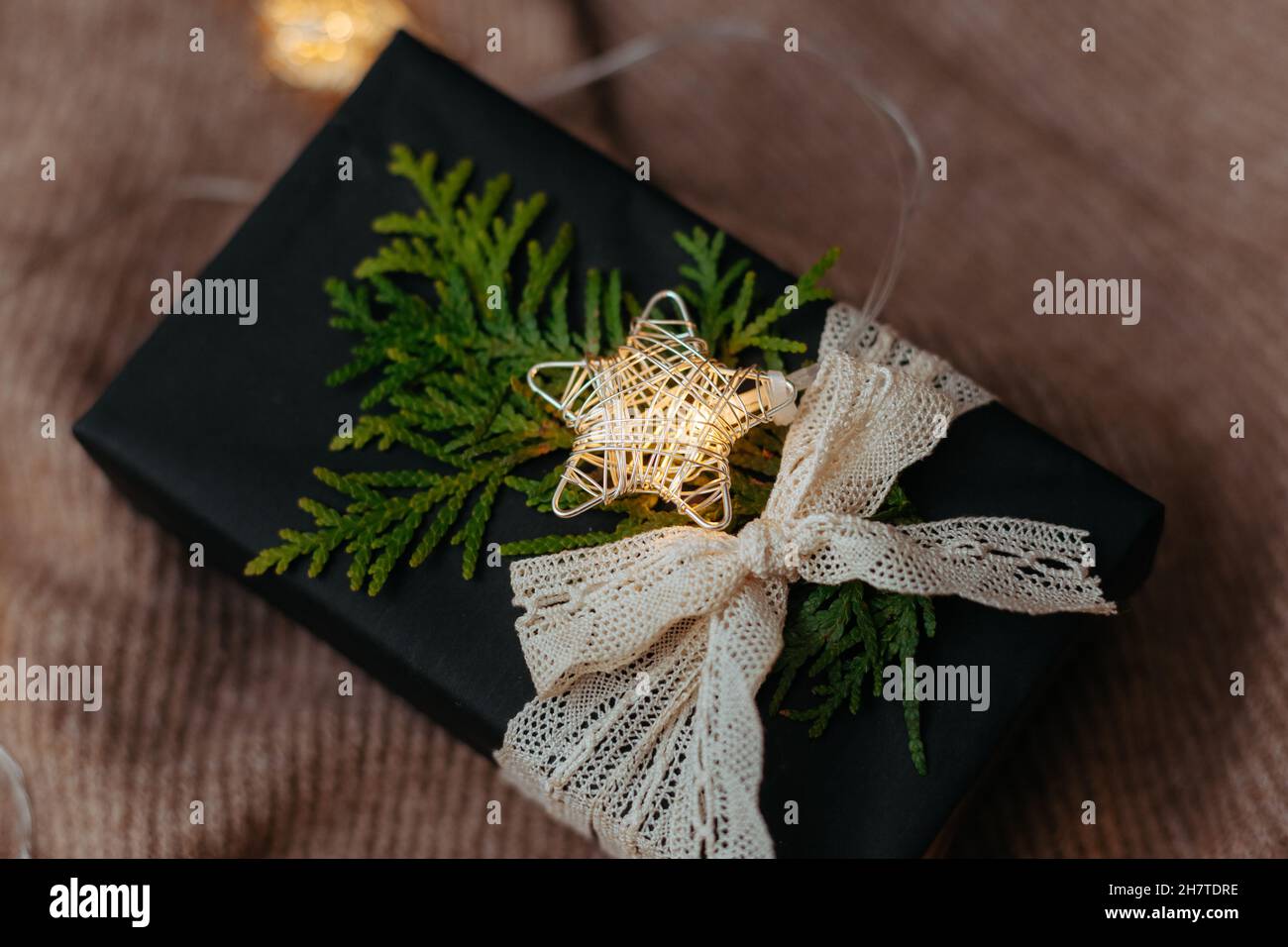 Regalo di Natale confezionato in carta da imballaggio nera adagiata su morbido sfondo di lana. Una ghirlanda luminosa per creare l'atmosfera di Capodanno Foto Stock