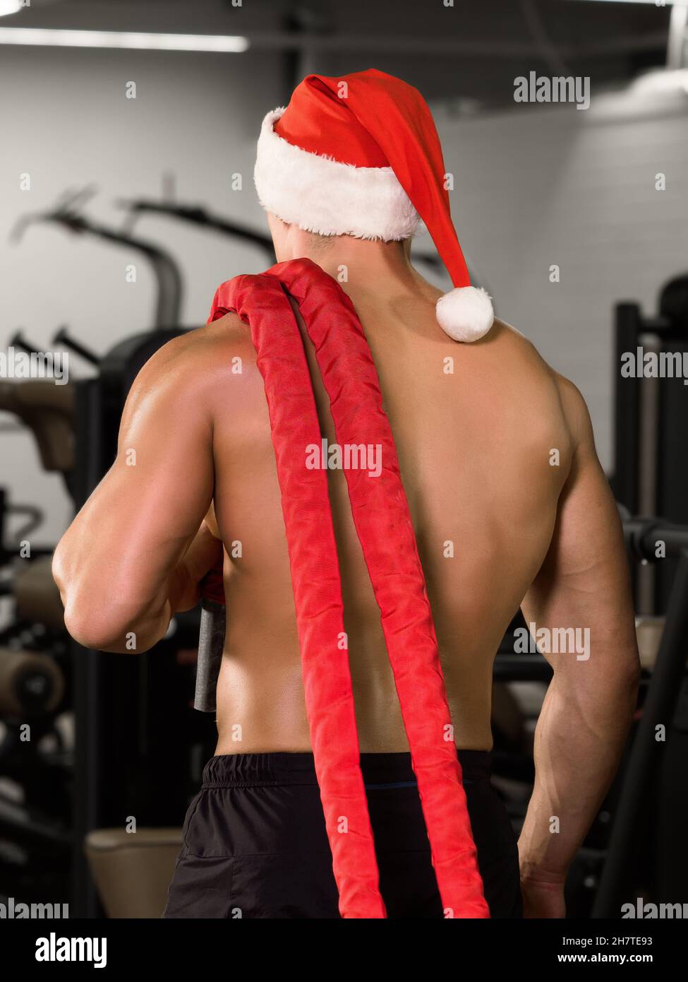 Bodybuilder muscolare in babbo natale cappuccio con corde sulla spalla in palestra Foto Stock