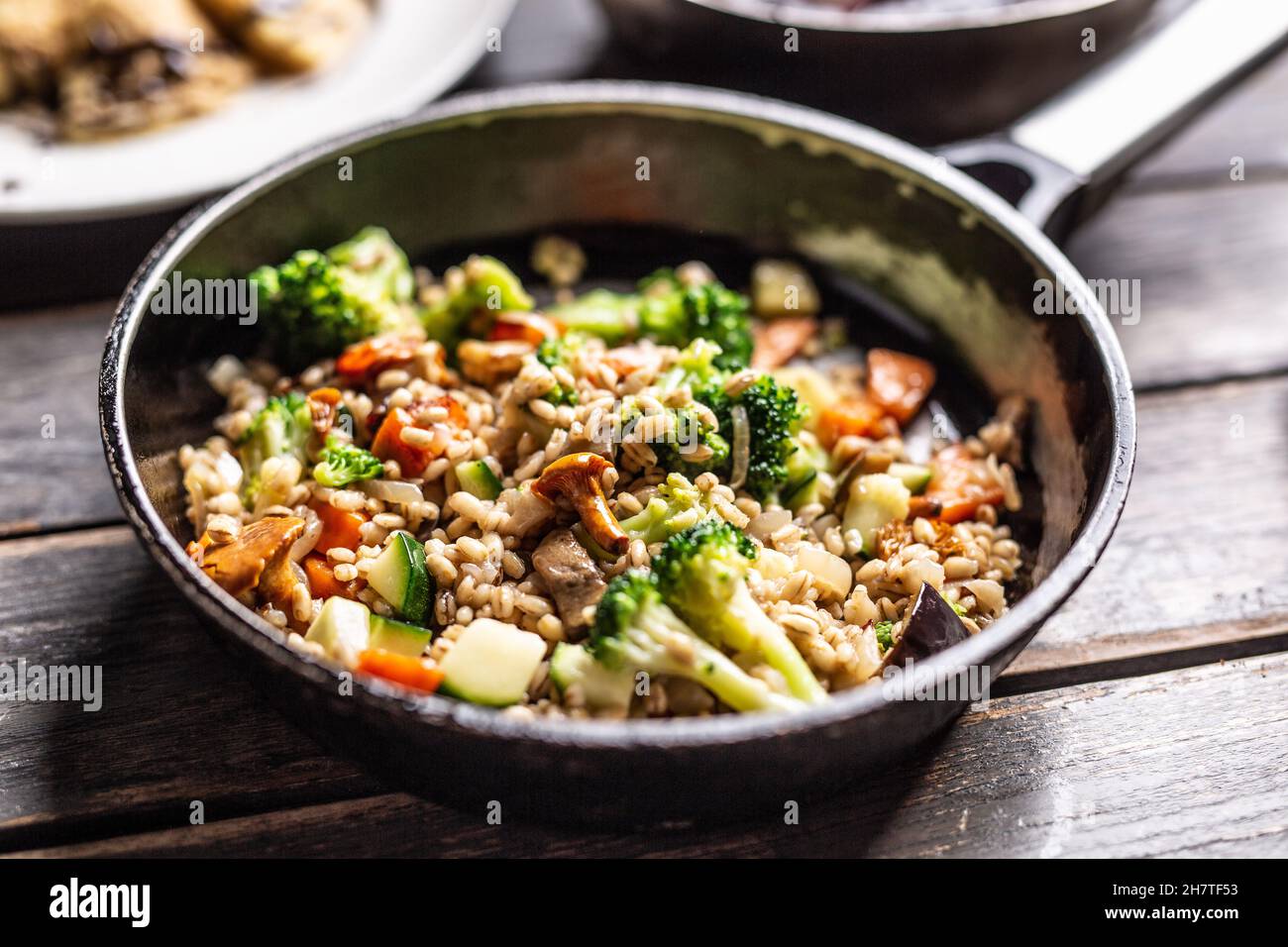 Pasto vegano sano di semole servito con broccoli, carote e funghi in una padella. Foto Stock