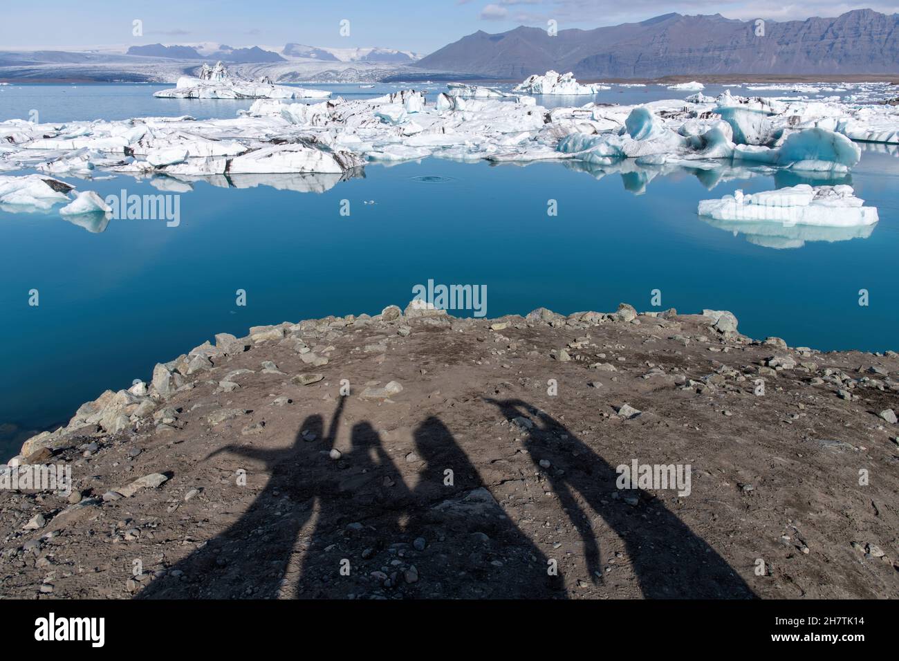 Ombra selfie di persone con le braccia sollevate al ghiacciaio Jokulsarlon, Islanda sullo sfondo delle acque della laguna glaciale; gente ombra la strada Foto Stock