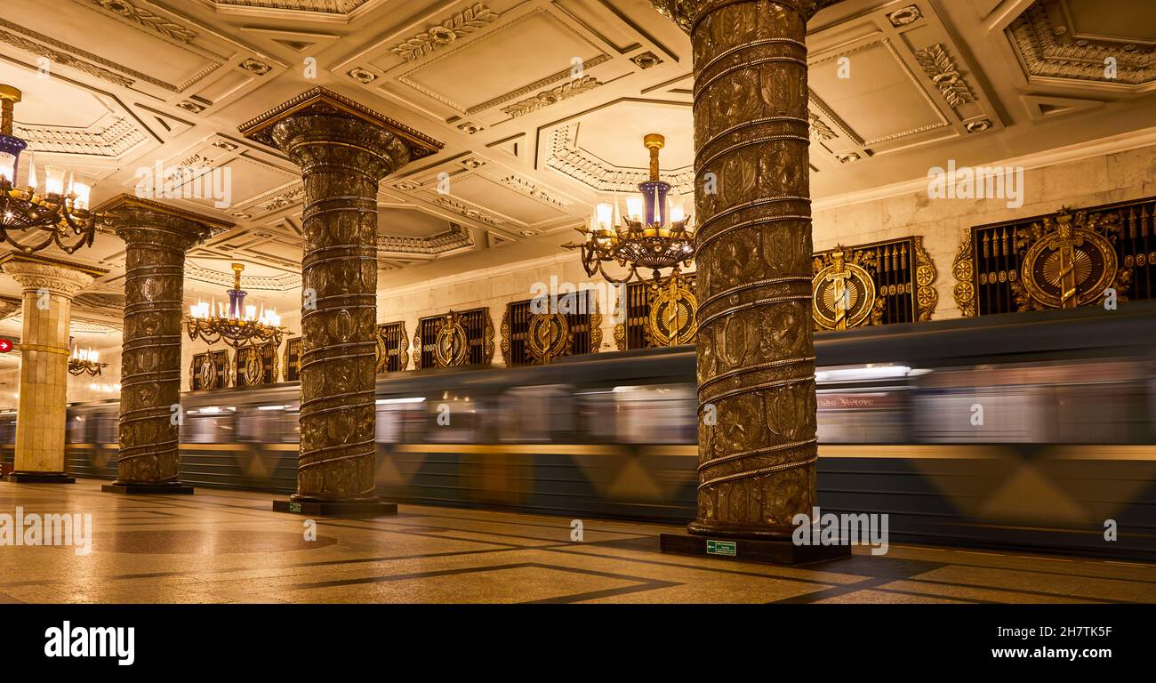 Lunga esposizione del treno della metropolitana che si muove in una stazione in vecchio stile con colonne scolpite e lampadari luminosi a Mosca Foto Stock