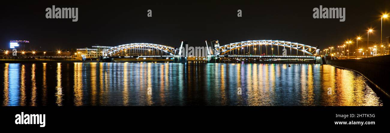 Vista panoramica del ponte ad arco illuminato con luci luminose che si riflettono sul fiume di notte a San Pietroburgo Foto Stock