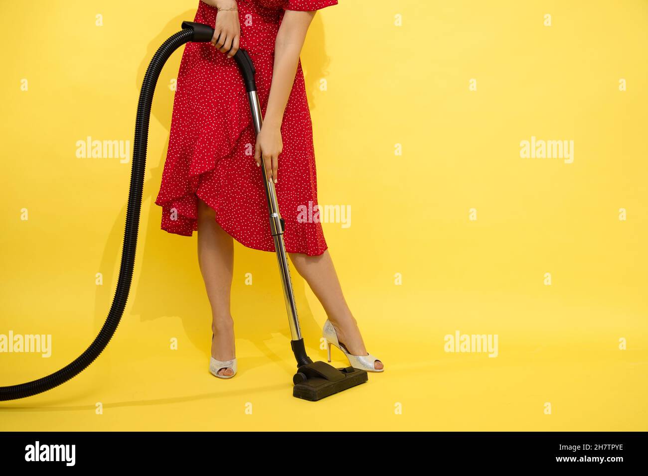 Foto di snella bella donna irriconoscibile in abito rosso su sfondo giallo tiene l'aspirapolvere in mani. Concetto di pulizia negli uffici, a ho Foto Stock