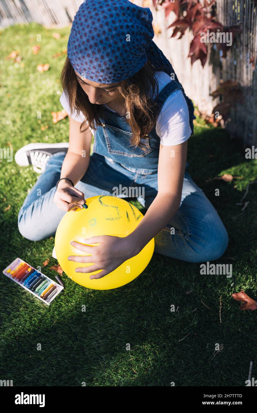 Ragazza attivista adolescente che dipinge un palloncino giallo in giardino in una giornata di primavera. Disegno di una chiamata per impedire che la temperatura della terra aumenti vicino Foto Stock