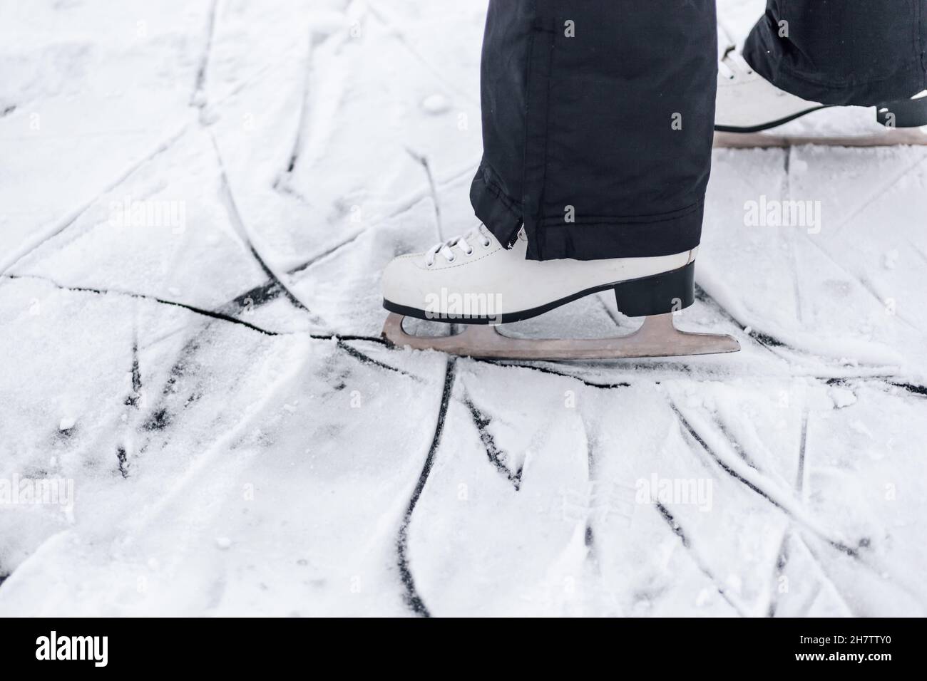 Foto ravvicinata dei pattini. Pattini di pattinaggio a figura bianca indossati sui piedi della persona, attingendo sul ghiaccio dalle lame dei pattini Foto Stock