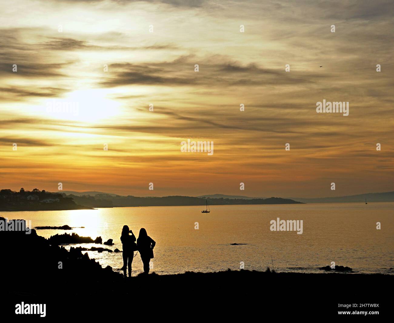 Silhouette di due ragazze che scattano foto del tramonto sul Mare d'Irlanda Foto Stock