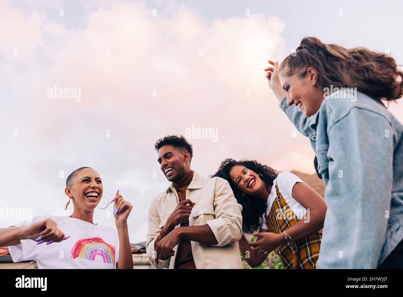 Quattro amici multiculturali che ballano sul tetto. Gruppo di giovani amici felici che ridono e si divertono durante una festa. Giovani vibranti h Foto Stock
