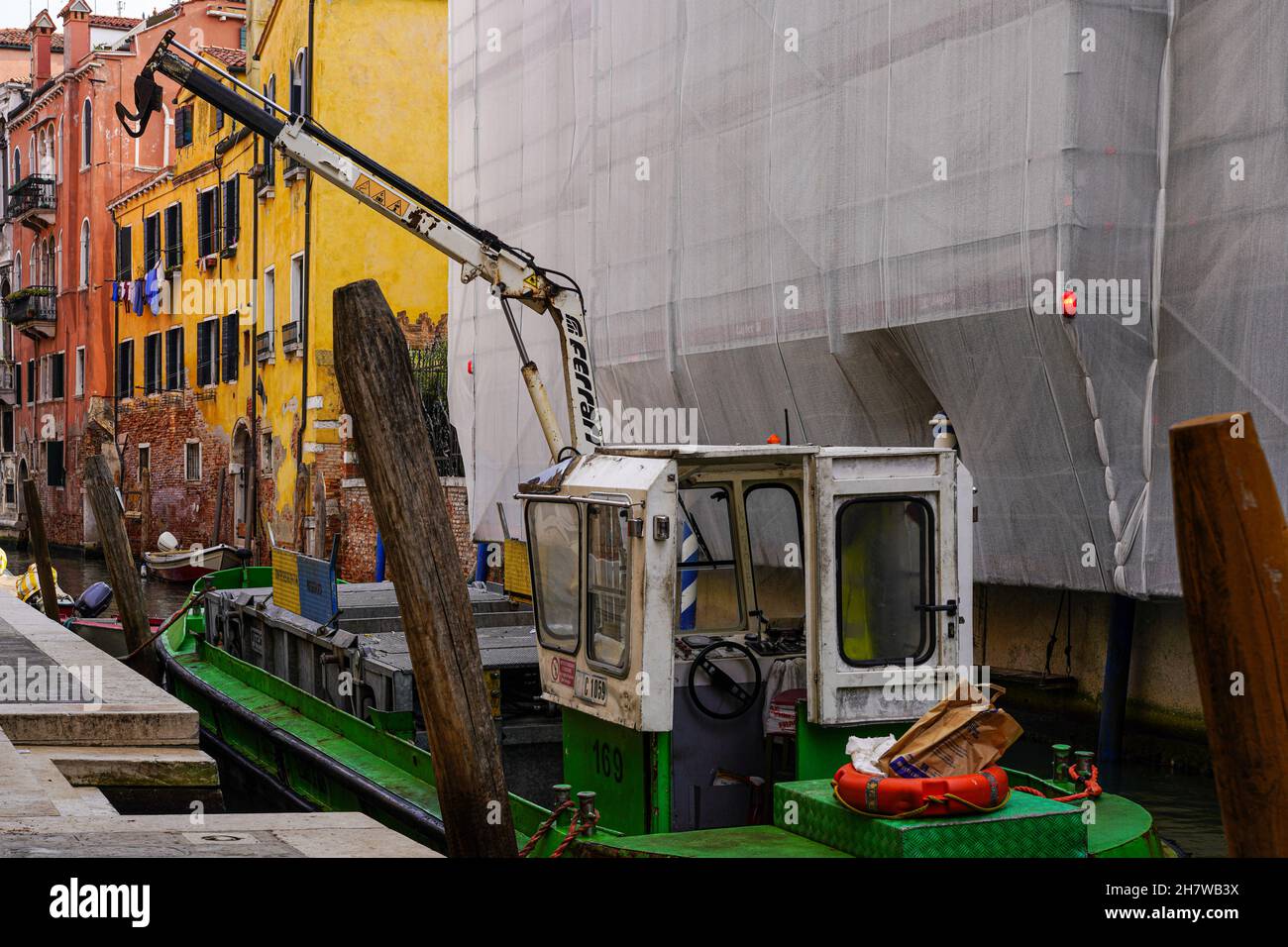 Una nave ha consegnato le merci in un cantiere in un piccolo canale di Venezia, che sono posti sul sentiero da una gru della nave. Foto Stock
