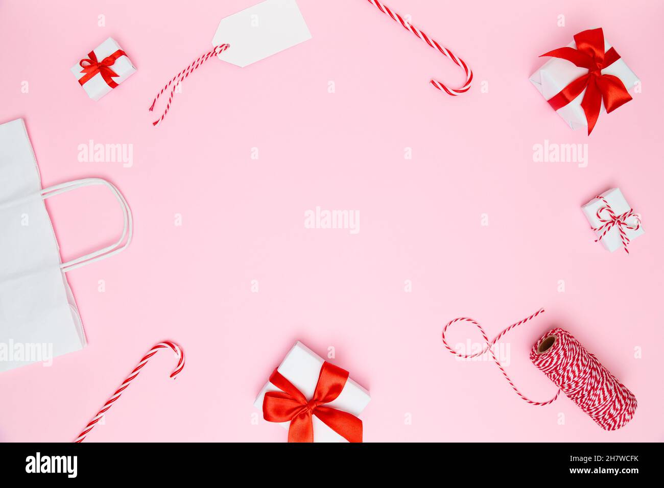 Natale, Capodanno sfondo accogliente. Scatole regalo bianche fatte a mano con archi rossi, sacchetto di carta, caramelle, nastro rosso, biglietto da visita su sfondo rosa pastello. Foto Stock