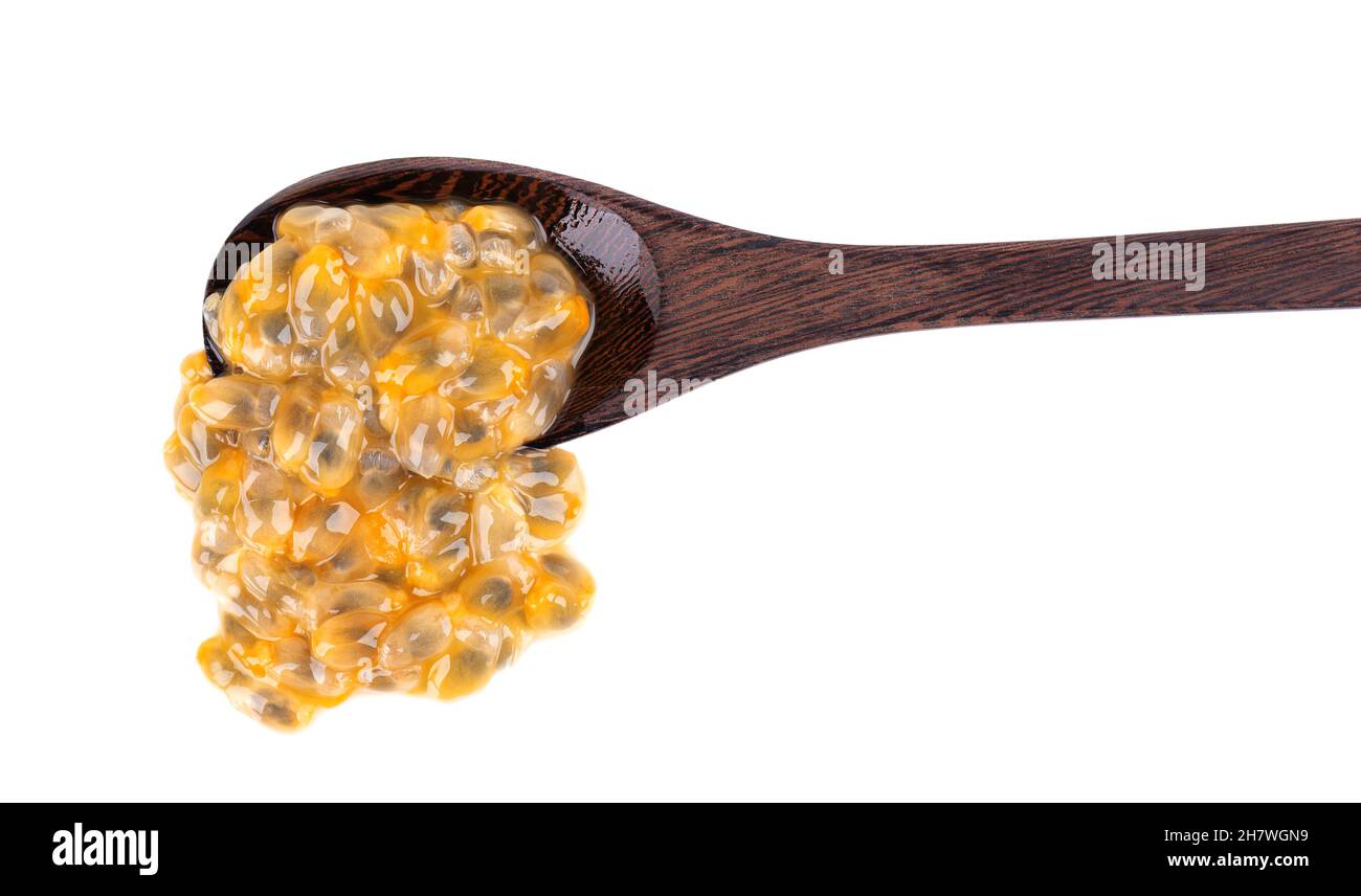 Semi di frutto della passione in cucchiaio di legno, isolato su sfondo bianco. Polpa di passionfrutto o maracuya, frutta esotica Foto Stock