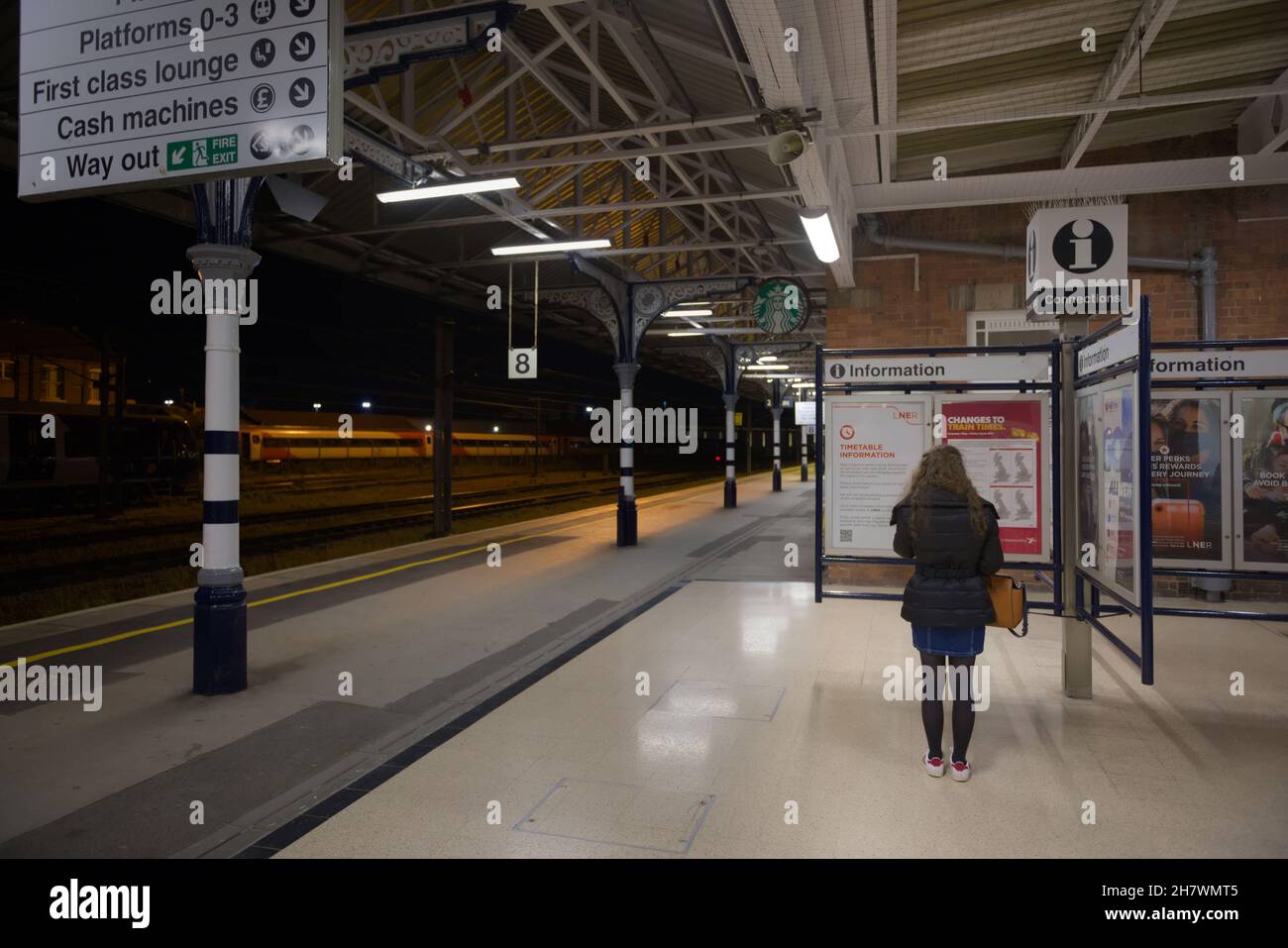 Doncaster, Regno Unito, 22 maggio 2021: Immagine grandangolare della piattaforma numero 8 della stazione ferroviaria di doncaster di notte. La donna legge il punto di informazione. Foto Stock