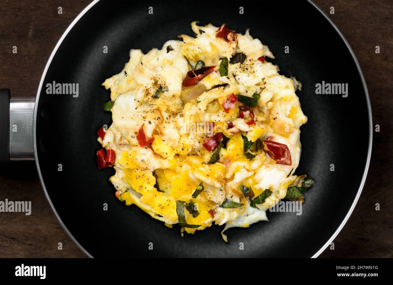 uova strapazzate su una padella nera su un tavolo di legno scuro, cotte con cipolla, peperoncini rossi, foglie di curry, piatto, vista dall'alto Foto Stock
