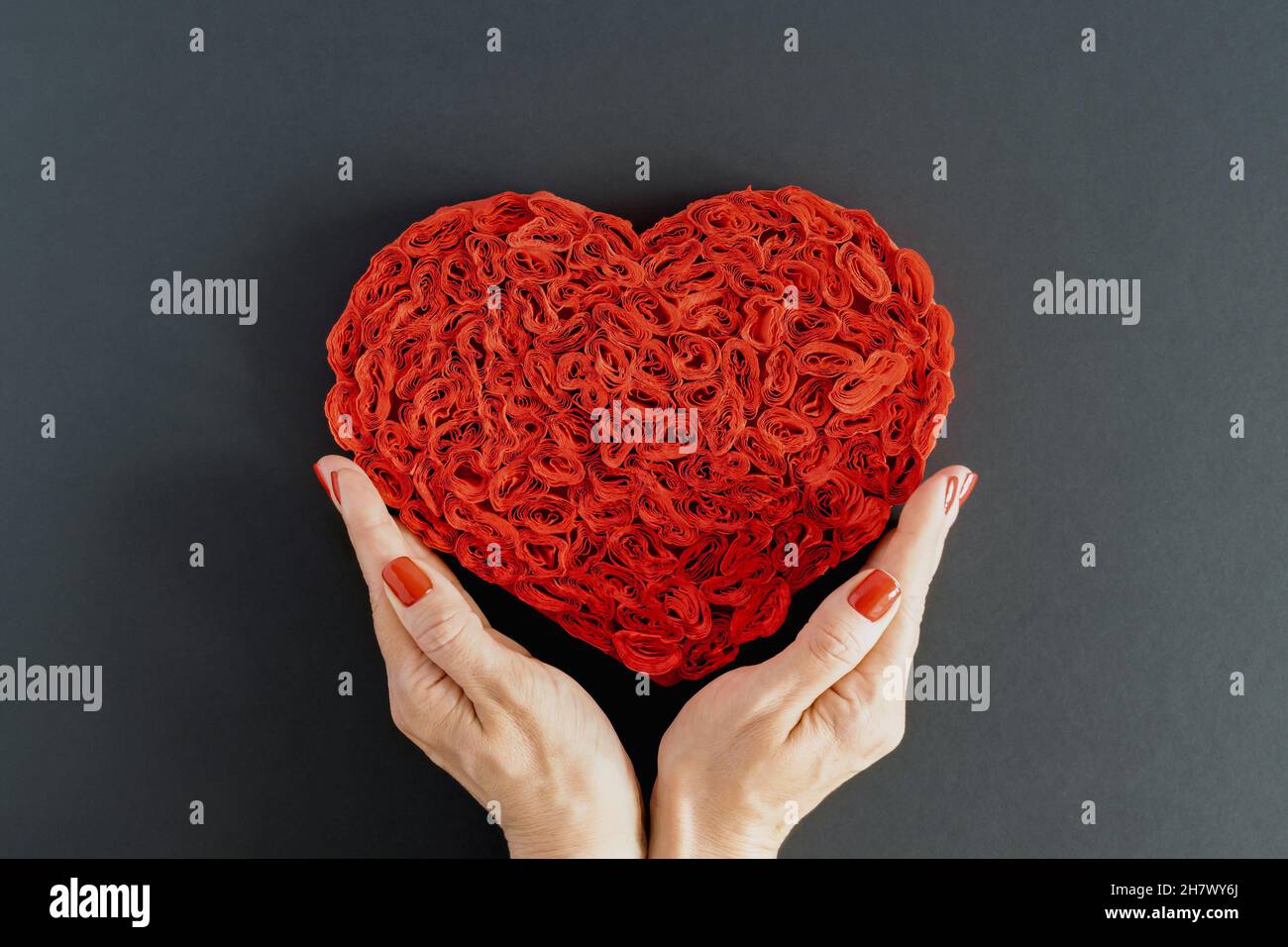 Cuore rosso in carta zaffinata su sfondo scuro nelle mani di una giovane donna. Il concetto di amore, dono, cura, Complimenti. Foto orizzontale. Foto Stock