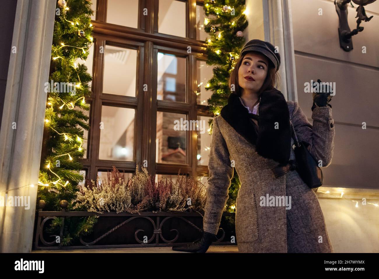 Natale, Capodanno outdoor moda invernale. Donna che cammina sulla strada della città decorata con le vetrine delle luci. Borsetta elegante da donna Foto Stock