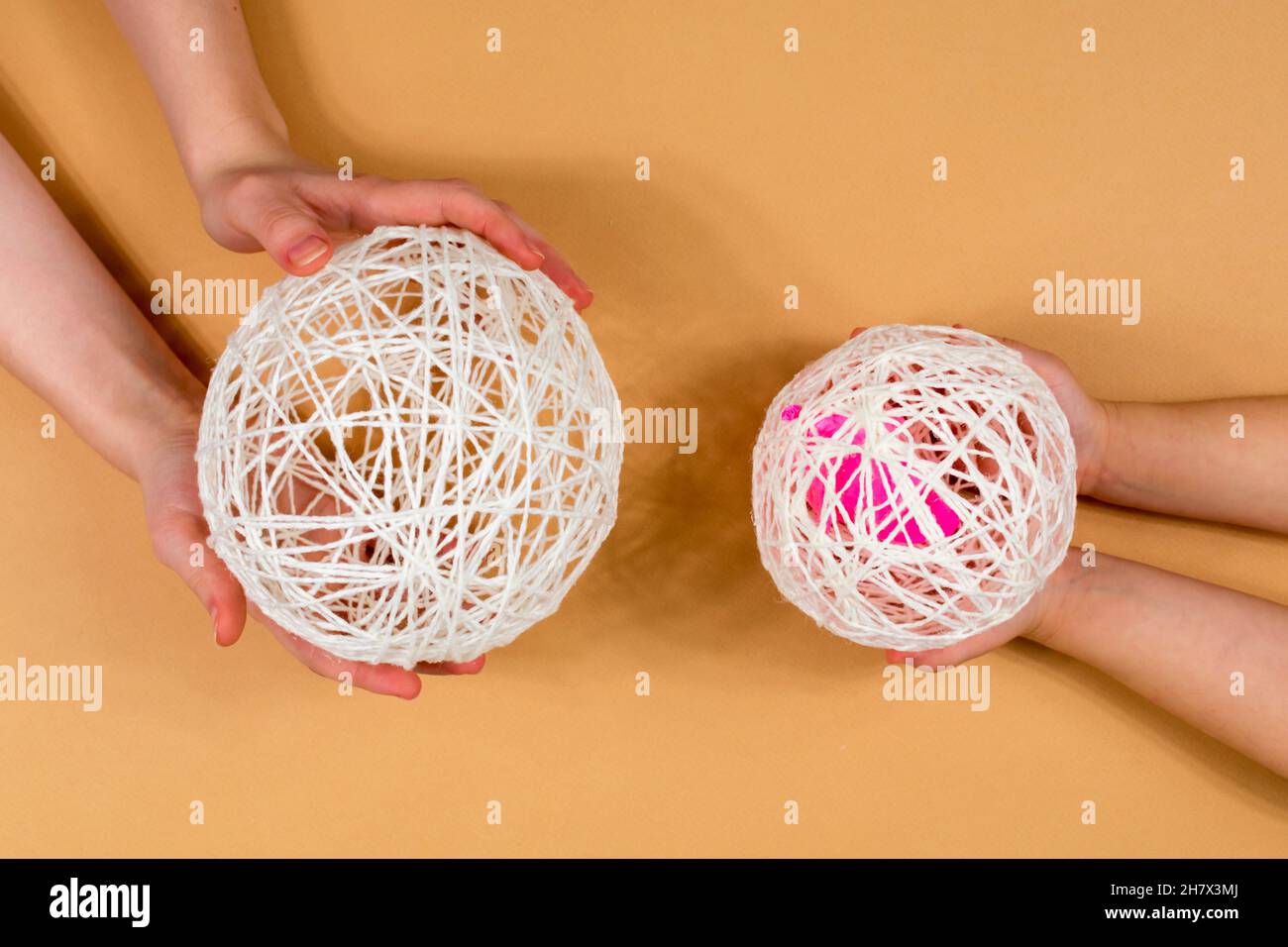Snowman fatto di fili. Le mani di bambini e adulti tengono palle di fili. Un insieme di articoli per fare un pupazzo di neve fatto a mano. Filettature, sfere, colla. Fase 4. Foto Stock