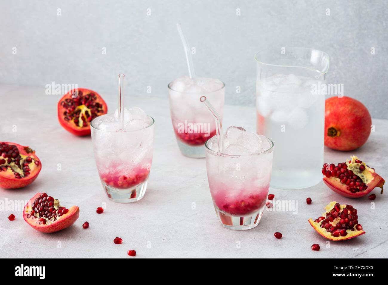Rinfrescante melograno bere in bicchieri con semi di melograno e ghiaccio, brocca di acqua fredda con agrumi, melograni tagliati con semi Foto Stock
